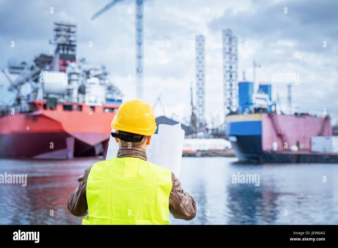 Ingénieur de construction navale la vérification des documents et des plans de construction sur le quai dans un port. Le port de casque de sécurité et gilet jaune, holding folded pa Banque D'Images