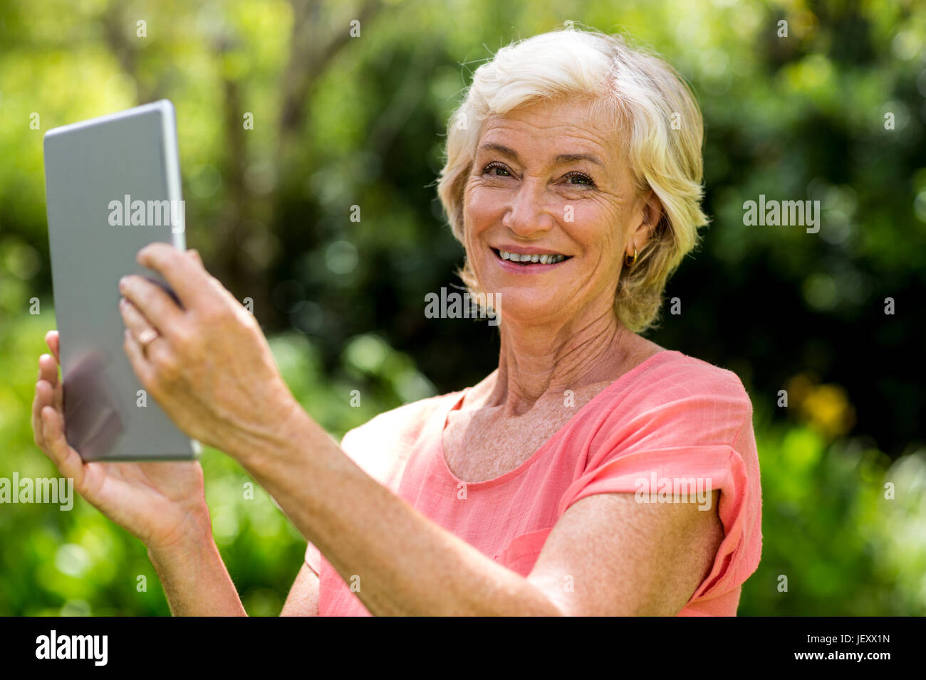 Smiling senior woman holding tablet in yard Banque D'Images