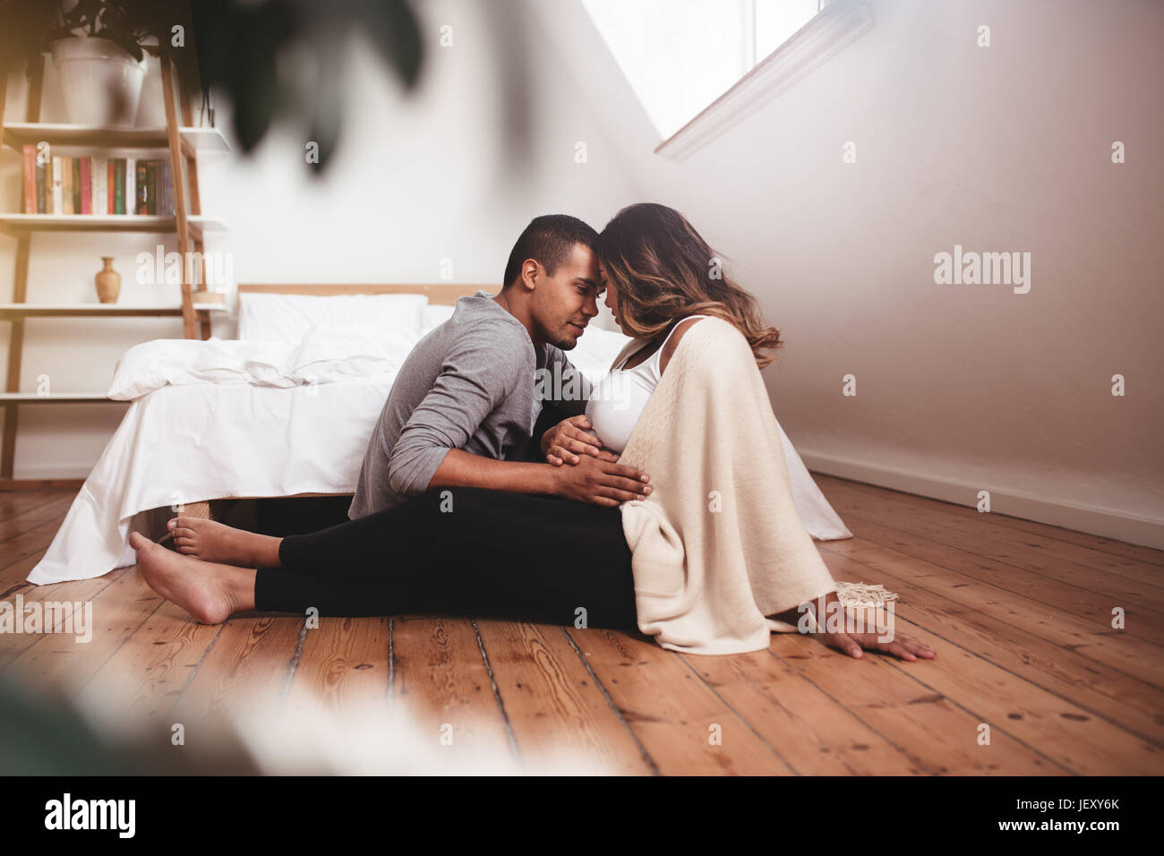 Romantique jeune couple assis sur le sol. Homme et femme attendant un bébé. femme enceinte avec mari se relaxant à la maison, tenant les mains sur le ventre. Banque D'Images
