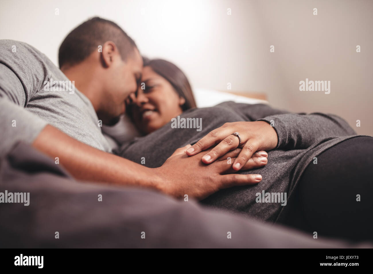 Young man and woman lying on bed, l'accent sur les mains sur le ventre. Enceinte africaine expecting. Banque D'Images