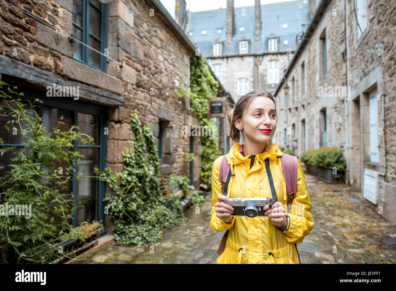 Jeune femme en imperméable jaune marche avec sac à dos et appareil photo à  Dinan village à la région Bretagne en France Photo Stock - Alamy