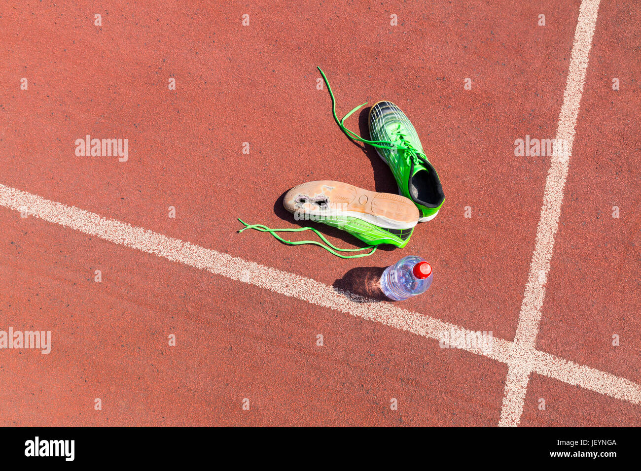 Une paire de chaussures de course verte cassée avec de grands trous dans l'unique portant sur une piste de course en plus d'une bouteille d'eau. Banque D'Images