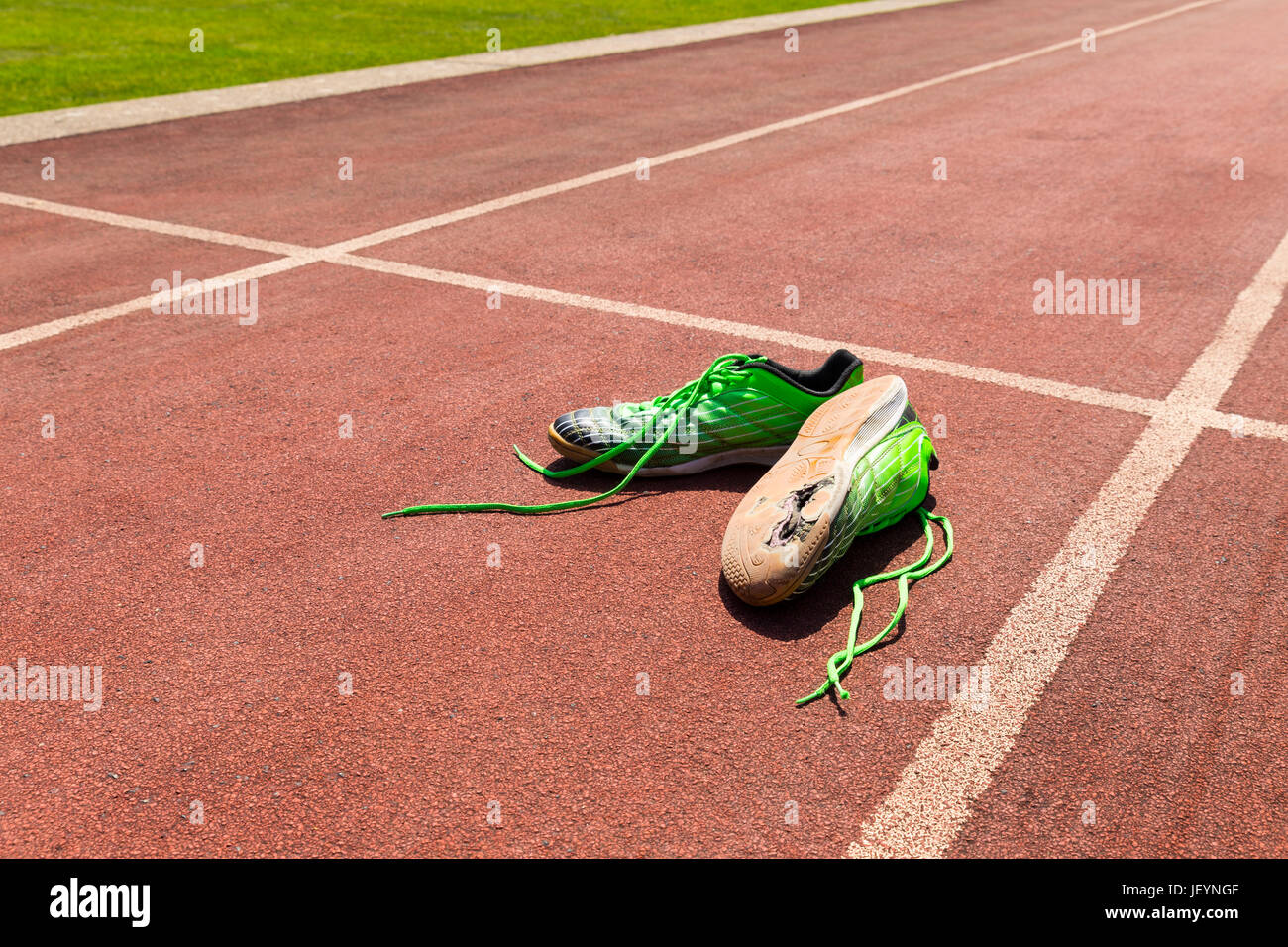 Une paire de chaussures de course verte cassée avec de grands trous dans l'unique portant sur une piste de course Banque D'Images