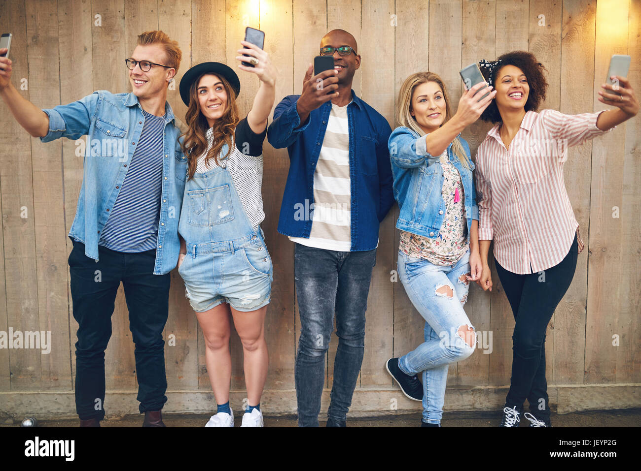 Joyeux groupe d'amis en noir et blanc en tenant debout à la selfies mur en bois et de sourire. Banque D'Images