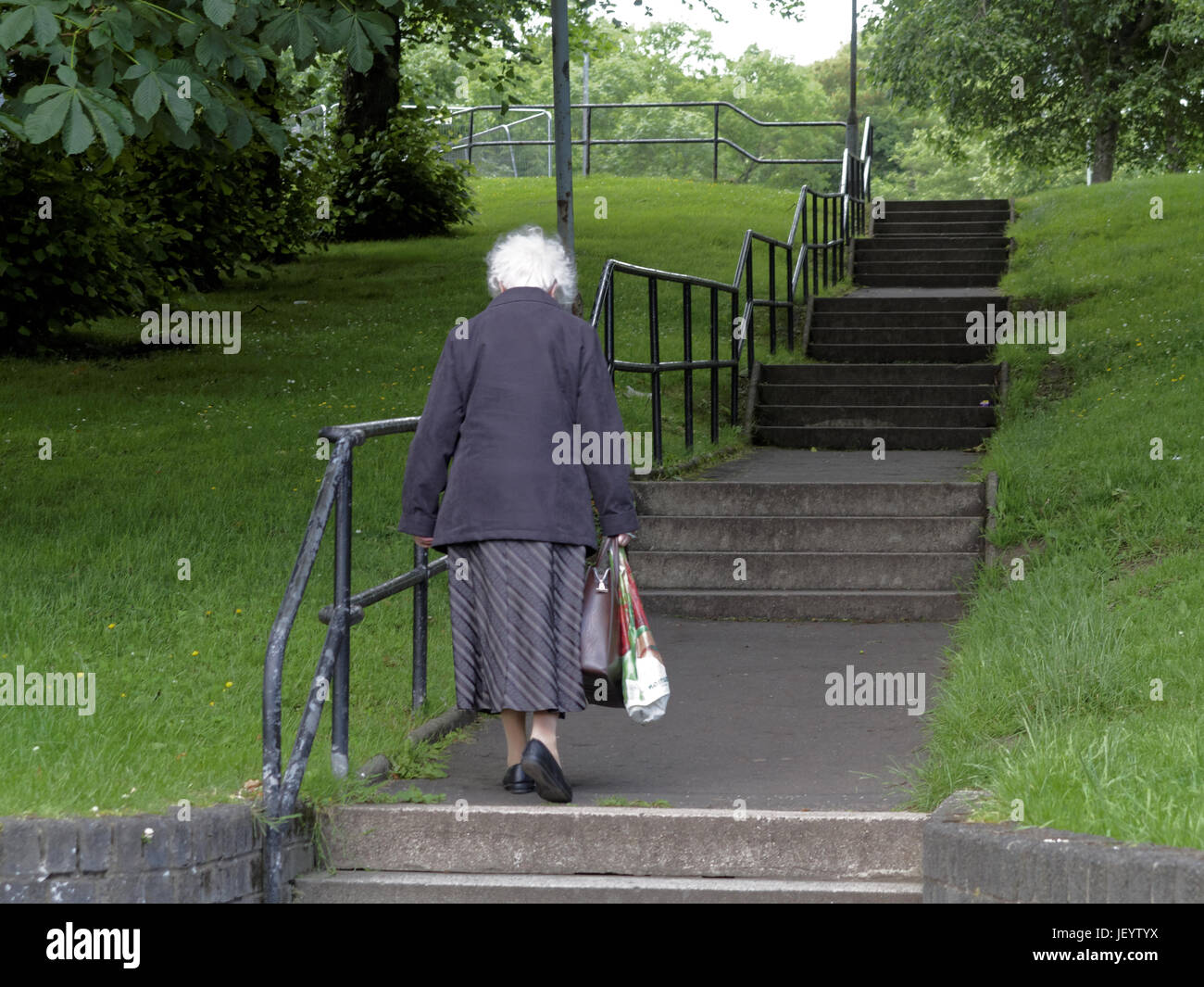 Personne âgée ou les aînés à Glasgow en Écosse de marcher seul vers le haut des escaliers en stationnement carrying shopping bags Banque D'Images