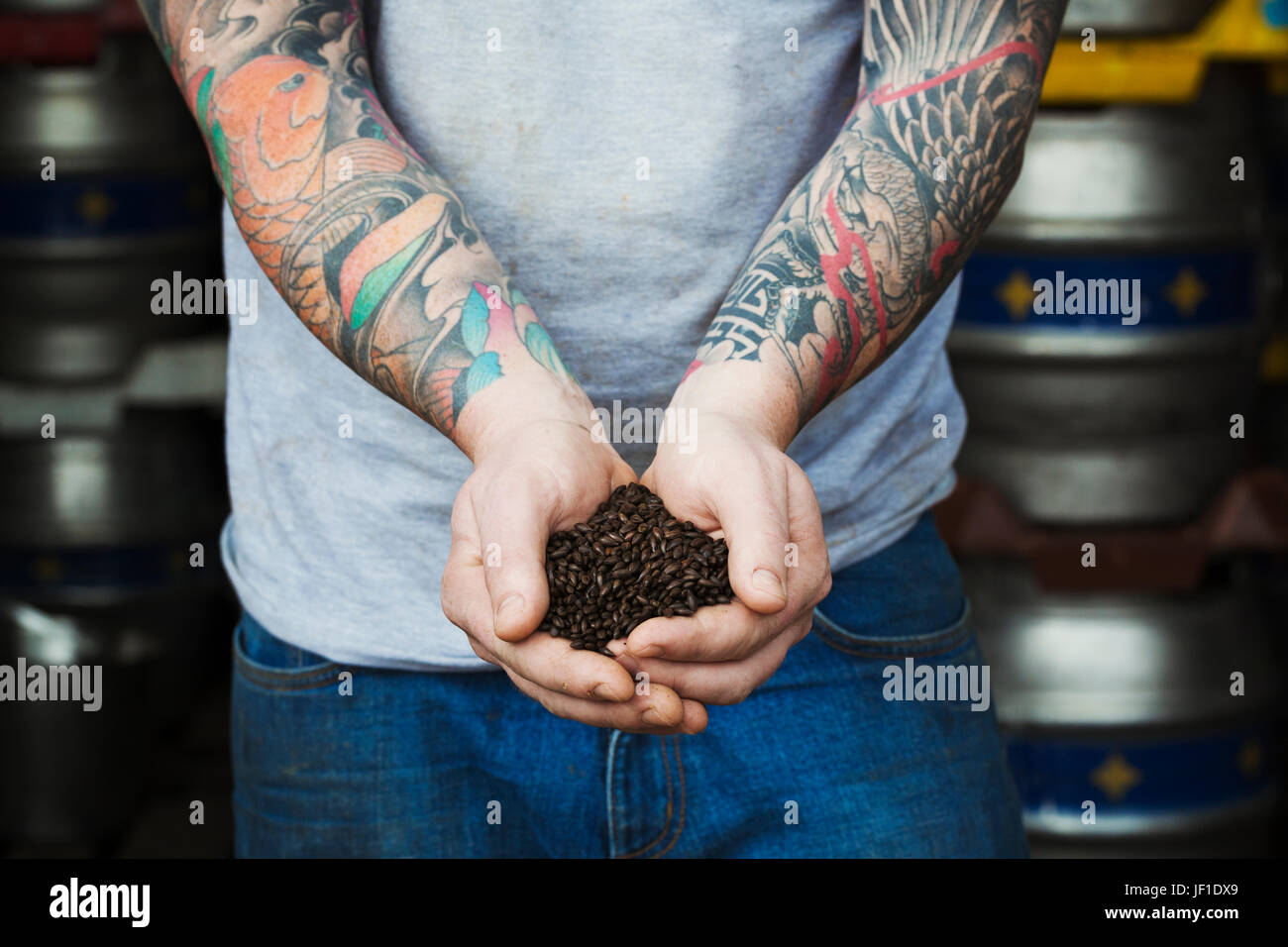 Close up of man standing dans une brasserie, contenant un malt brun foncé, tattoed armes. Banque D'Images