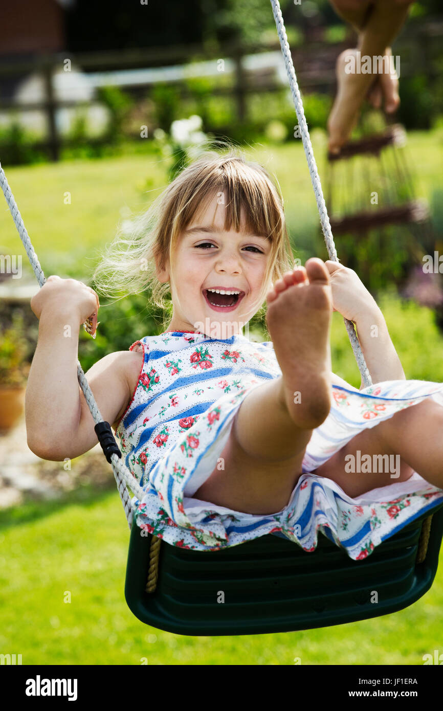 Jeune fille souriante portant une robe d'été sur une balançoire dans un jardin. Banque D'Images