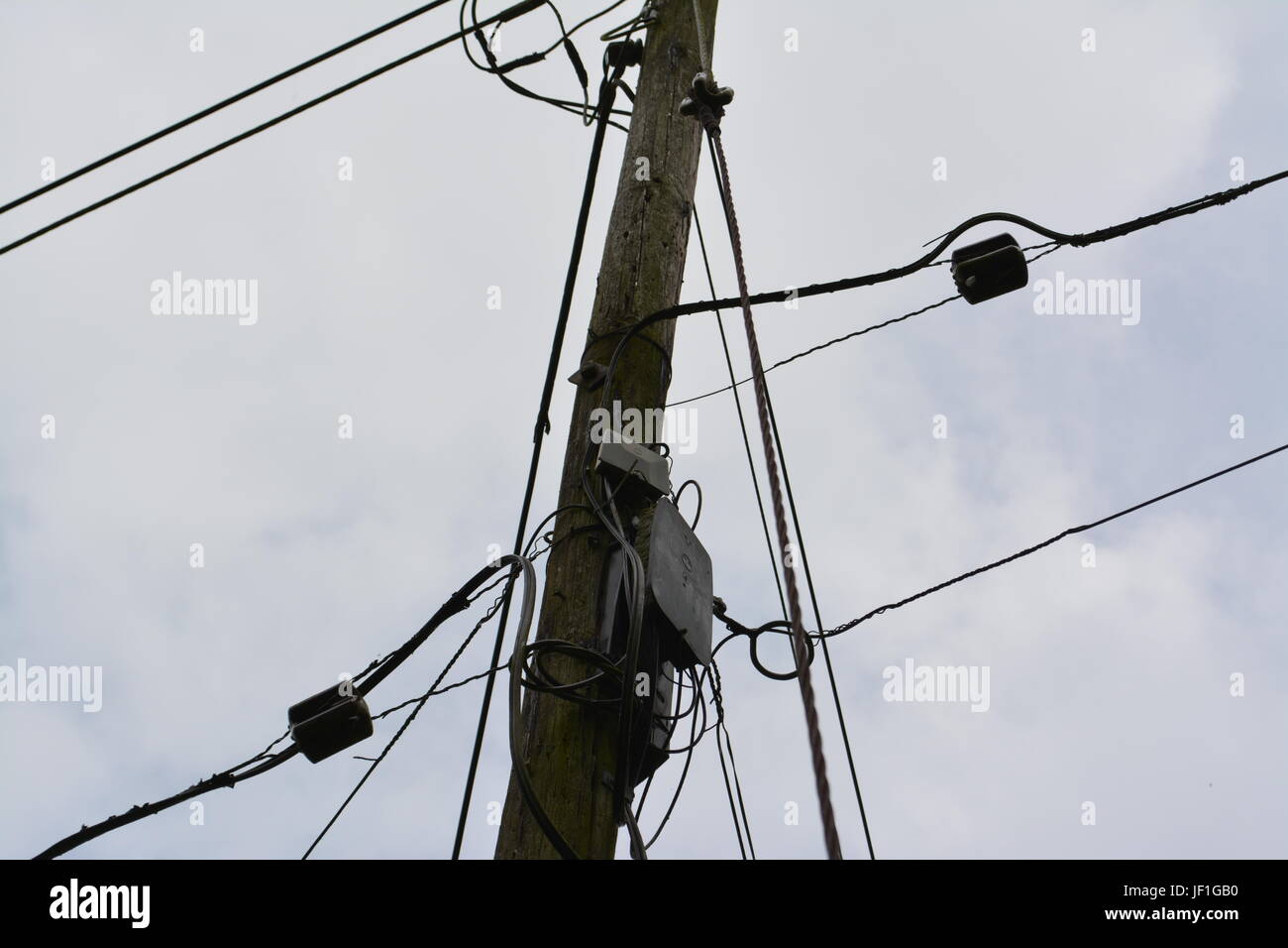 Close up d'électricité et de câbles téléphoniques fils sur poteau en bois bois avec ciel couvert ciel nuageux gris en arrière-plan l'Angleterre UK Banque D'Images