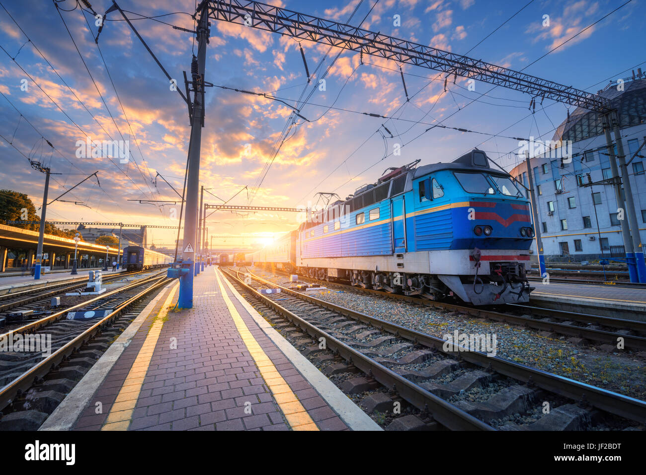 Le train bleu à la gare de chemin de fer au coucher du soleil. Paysage industriel étonnant avec vieille locomotive, vieux bâtiments, des rails et de soleil colorés sky avec le cloud Banque D'Images