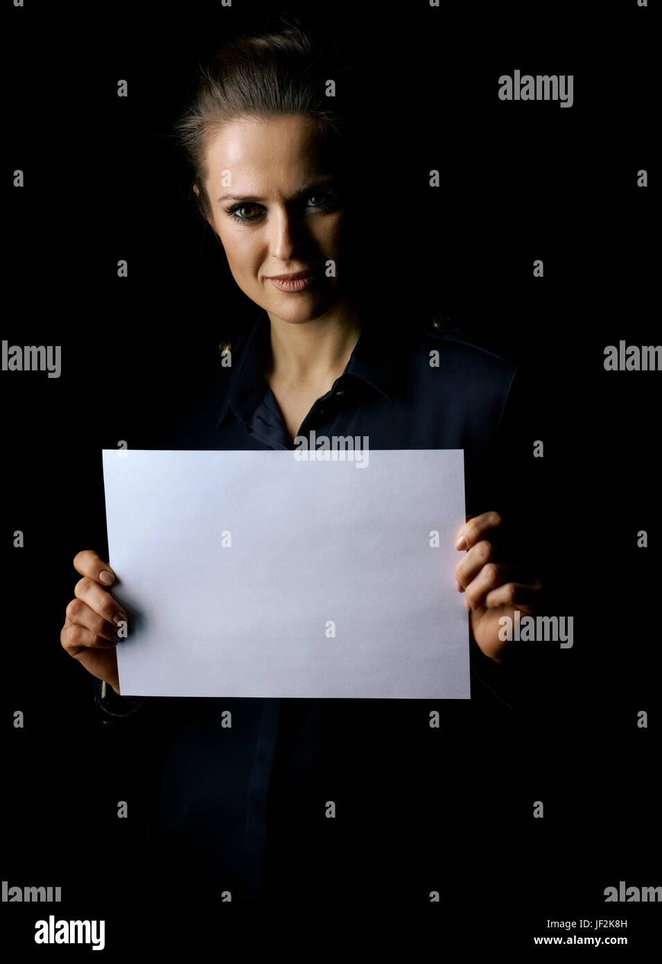 Сoming dans la lumière. Portrait de femme à la robe sombre isolé sur fond noir montrant le papier vierge sheet Banque D'Images