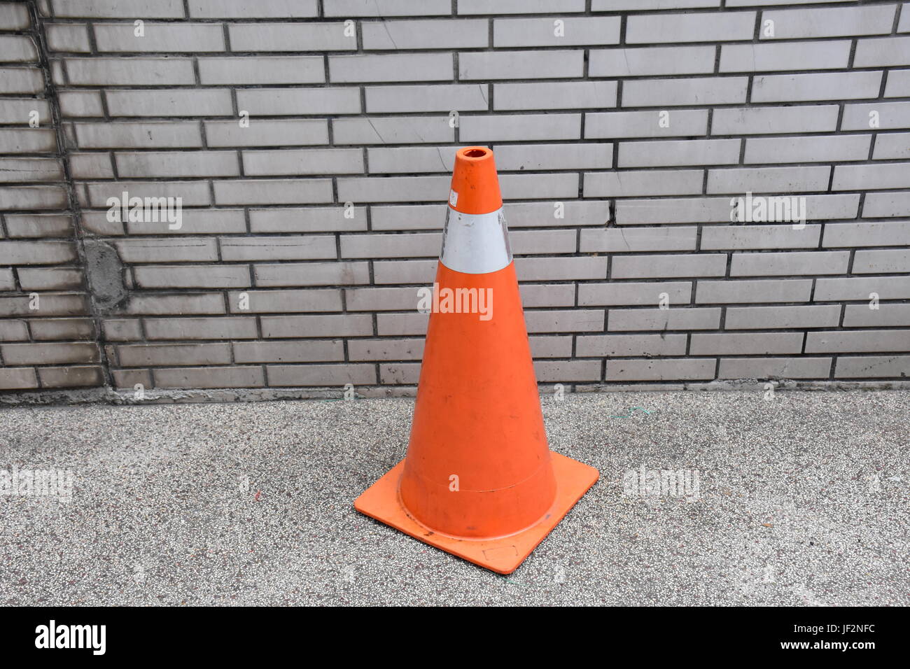 Un seul cône d'avertissement près d'un mur le long d'un trottoir gardé là pour réserver une place de parking pour un scooter. Banque D'Images