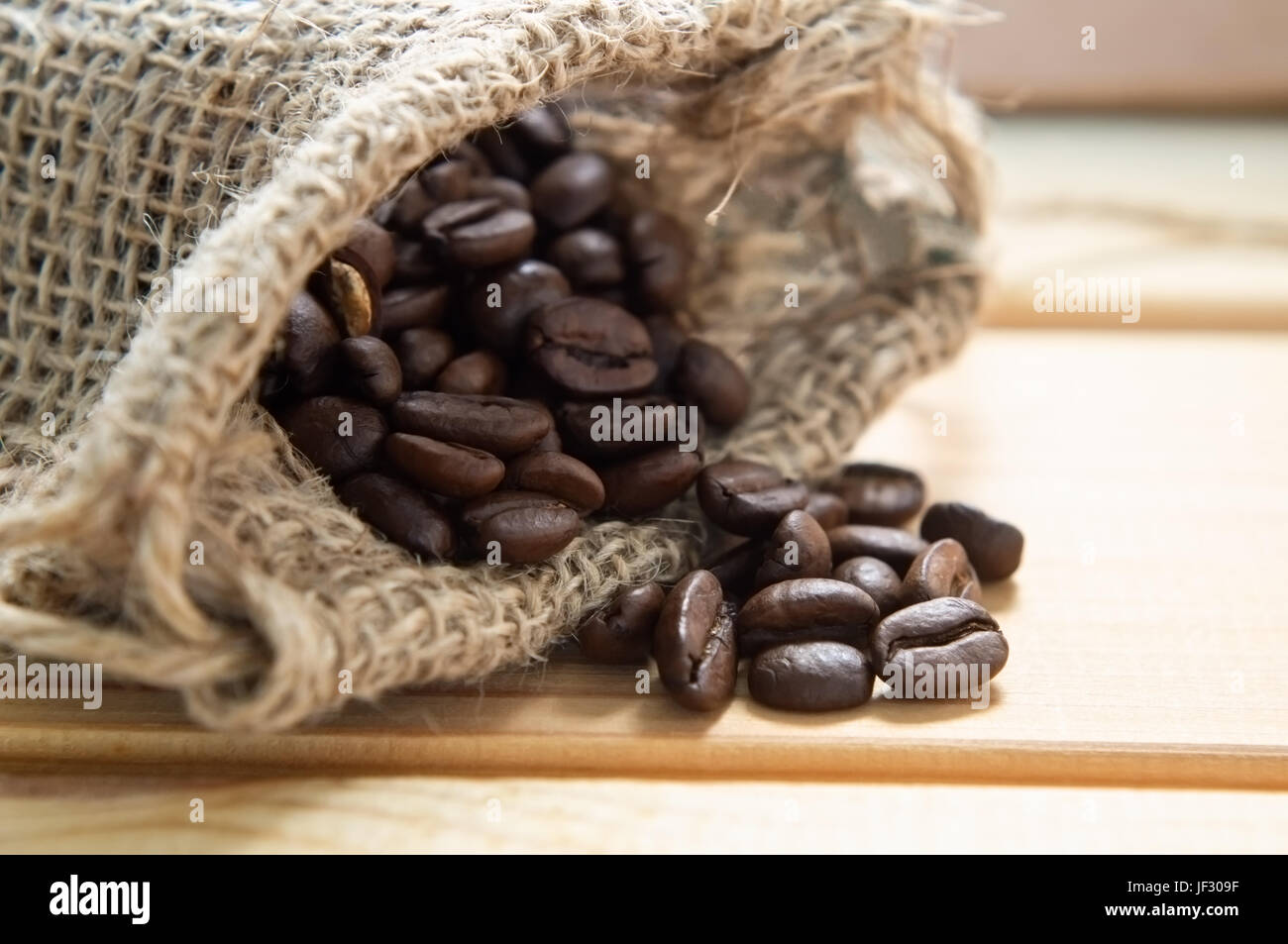 Close up d'un sac en toile de jute contenant les grains de café, déversant sur table en bois. Banque D'Images