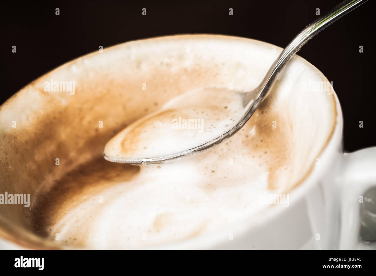 Cappuccino. Mousse de lait dans la cuillère sur fond noir Banque D'Images