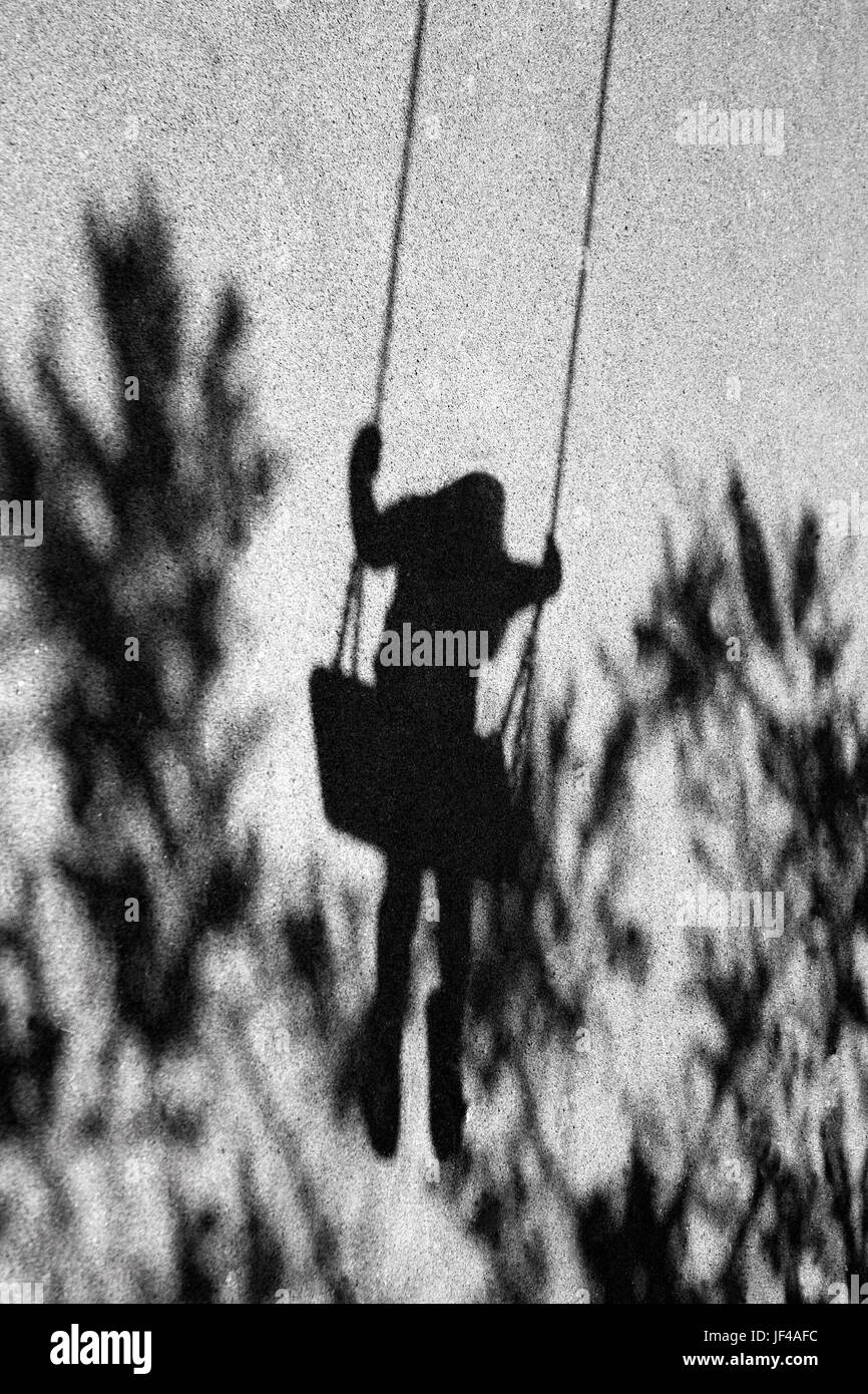 Ombres floues d'une fille sur une balançoire et une branche d'arbre dans la ville aire de jeux Banque D'Images