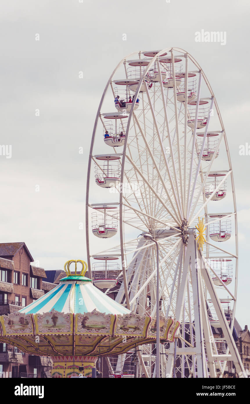 Grande roue sur fond de ciel gris, merry go round en premier plan. Banque D'Images