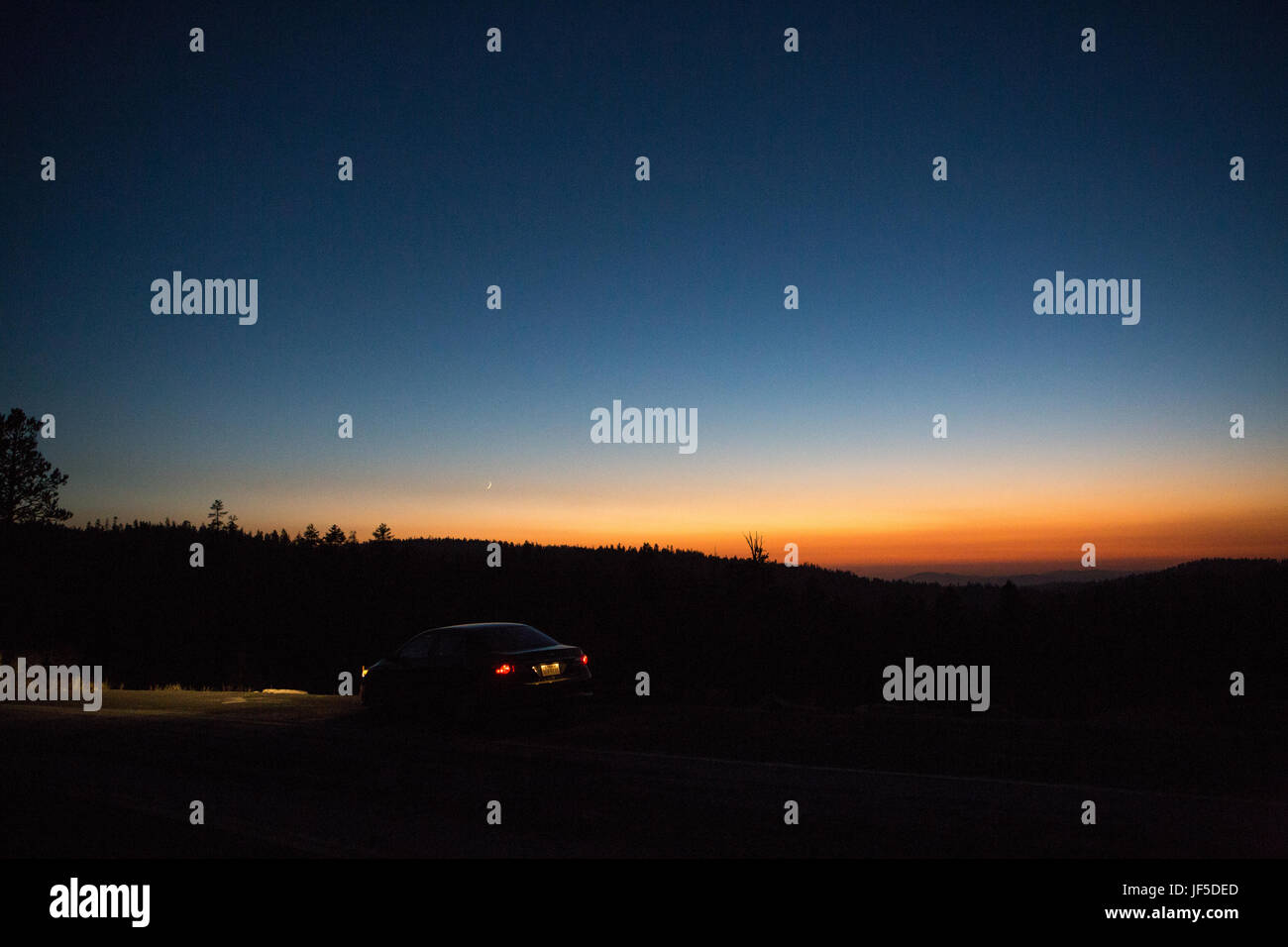 Au crépuscule, une voiture s'arrête sur le côté de la route comme une fine lanière de le croissant de lune est visible. Banque D'Images