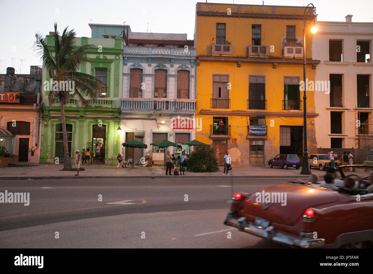 Au crépuscule, les gens debout sur la rue comme une voiture américaine classique par les lecteurs dans le centre-ville de La Havane. Banque D'Images