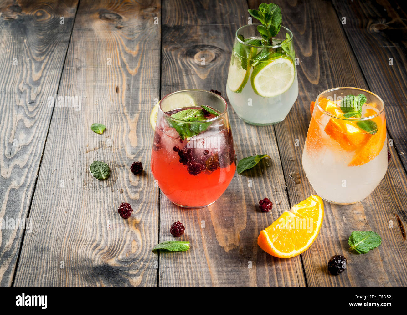 Sélection de trois sortes de gin tonic : avec les mûres, avec orange, avec de la chaux et de feuilles de menthe. Dans les verres sur un fond de bois rustique. Copy space Banque D'Images