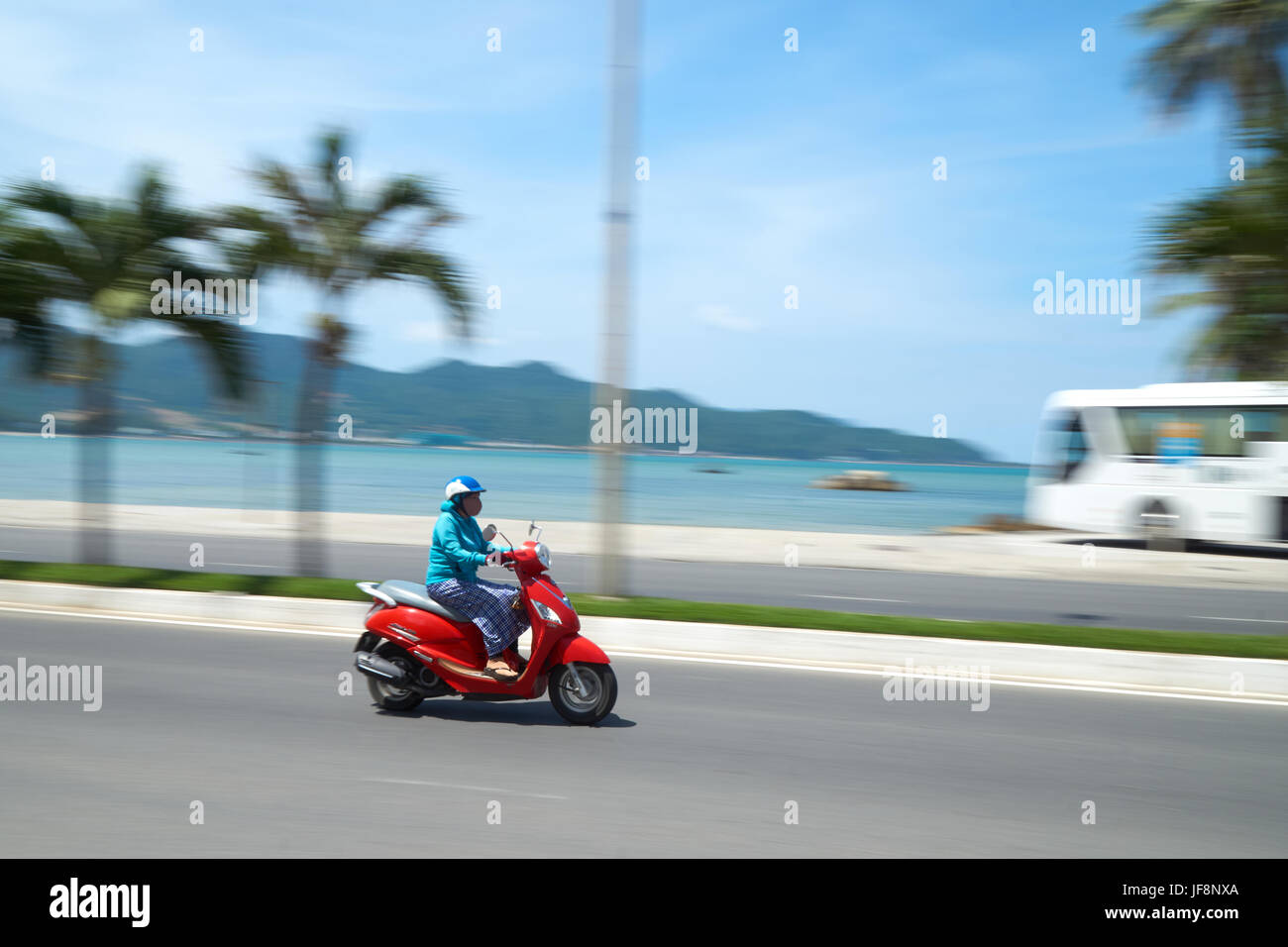 Pilote moto méconnaissable en face de la plage près de Nha Trang, Vietnam. Capturé en mouvement, floue. Avec un bus de tourisme en arrière-plan. Banque D'Images