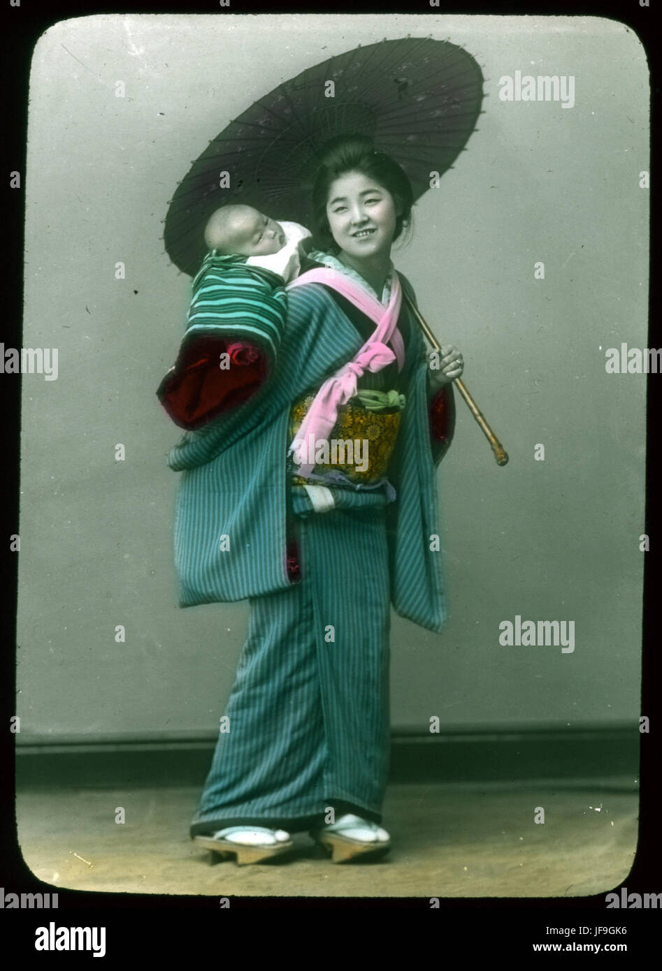 Photographie frappante d'une femme vêtue d'une robe traditionnelle de l'époque Meiji, tenant un parasol et un bébé, reflétant les coutumes sociales du Japon du XIXe siècle Banque D'Images