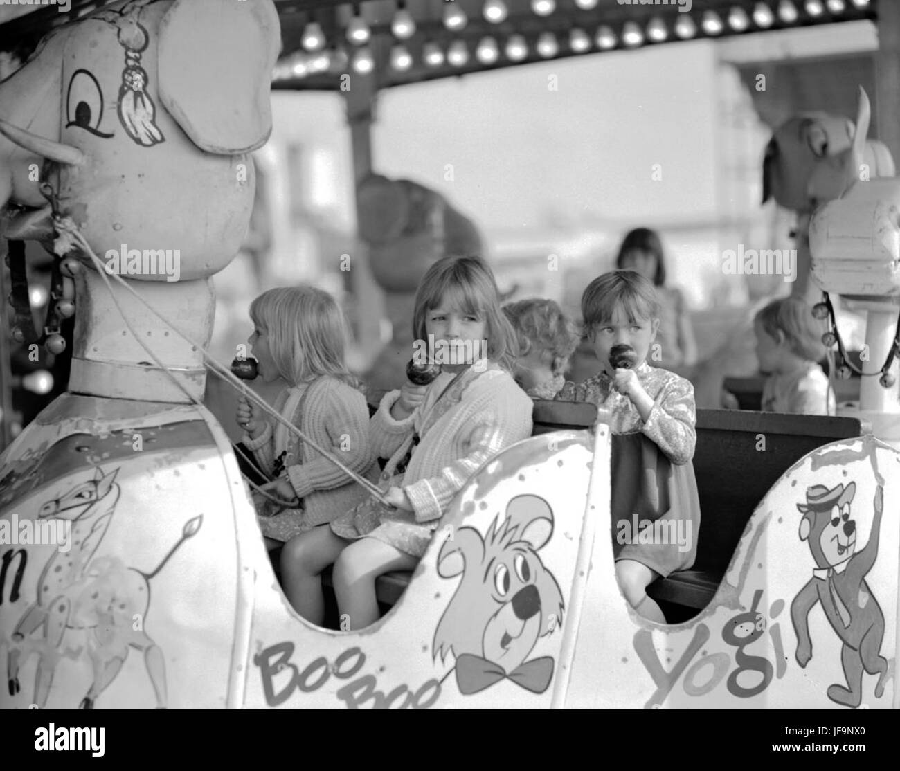 Une photographie vintage de personnes mangeant des pommes caramel à la foire Hoppings, un événement d'amusement traditionnel qui se tient chaque année à Newcastle upon Tyne. L'image met en valeur une atmosphère de foire funiculaire avec manèges, divertissements et plaisir familial. Banque D'Images