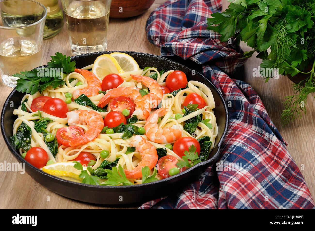 Pâtes aux crevettes frits, les pois, les tomates et les épinards dans une poêle, sur une table avec des verres de cidre. Banque D'Images