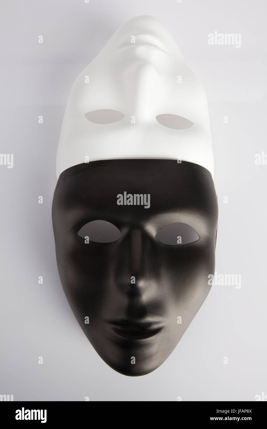Les masques noirs et blancs réunis sur fond réfléchissant blanc. Vertical image, vue du dessus. Concept de l'anonymat. Banque D'Images