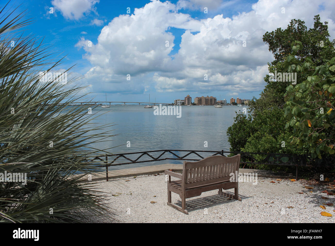 Banc en bois vide vous appelle s'asseoir et profiter de la vue sur la baie de Sarasota au pont, l'eau reflétant le ciel bleu et nuages blancs flottant. Banque D'Images