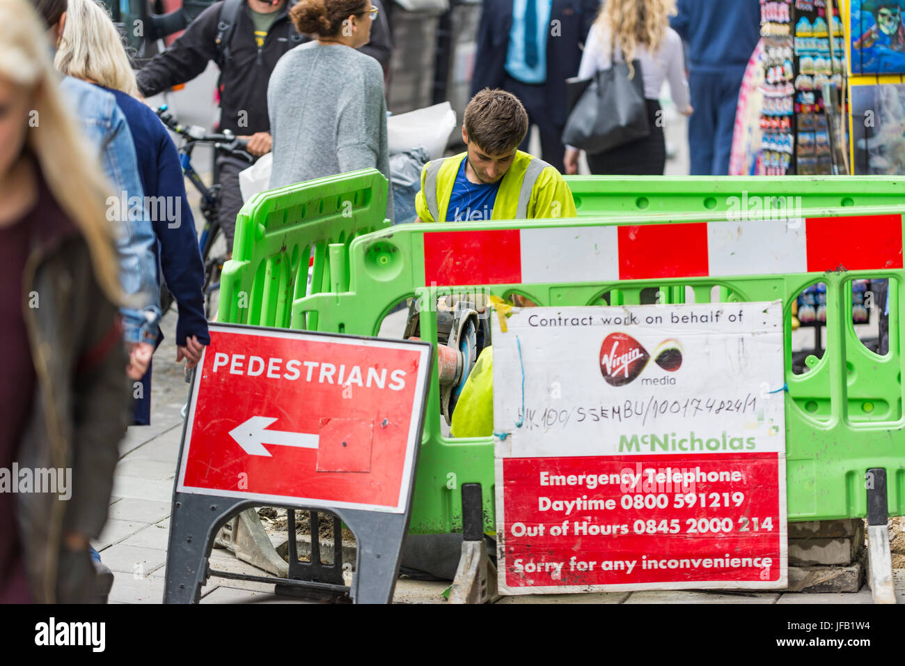 Travaux de la chaussée. Les travailleurs sur un trottoir au Royaume-Uni avec des barrières de diriger les piétons autour de lui. Banque D'Images