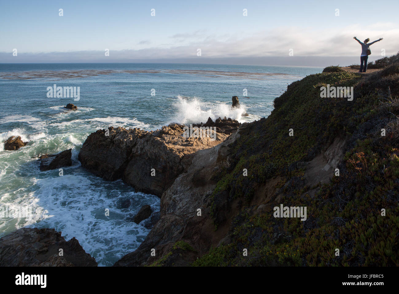 Un touriste sur une formation rocheuse à l'océan Pacifique. Comme les vagues déferlent sur les rochers, elle étend ses bras dans l'excitation. Banque D'Images