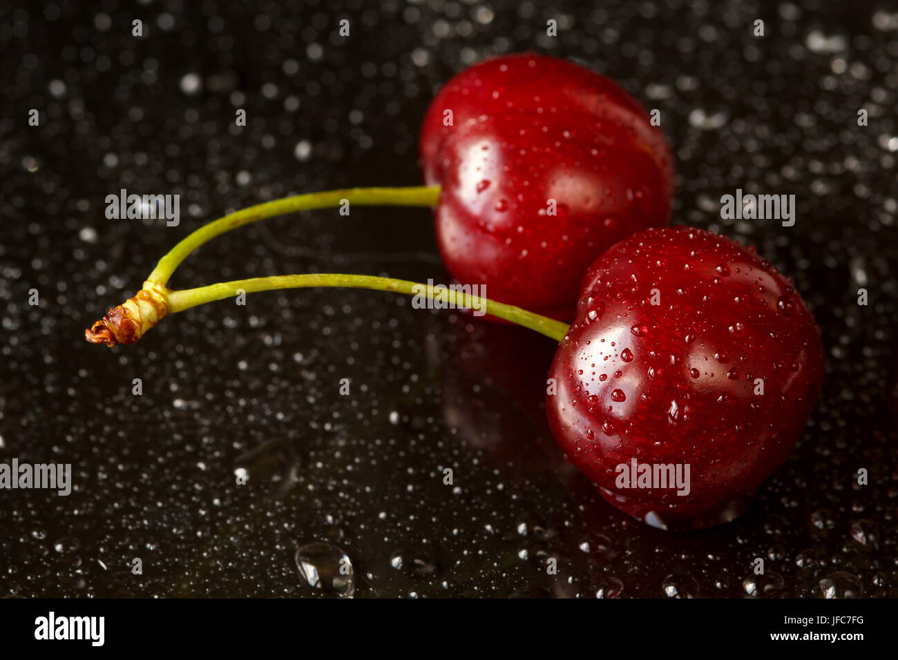 Plan Macro sur deux délicieuses cerises mûres sur un fond réfléchissant noir avec des gouttes d'eau. Profondeur de champ Banque D'Images