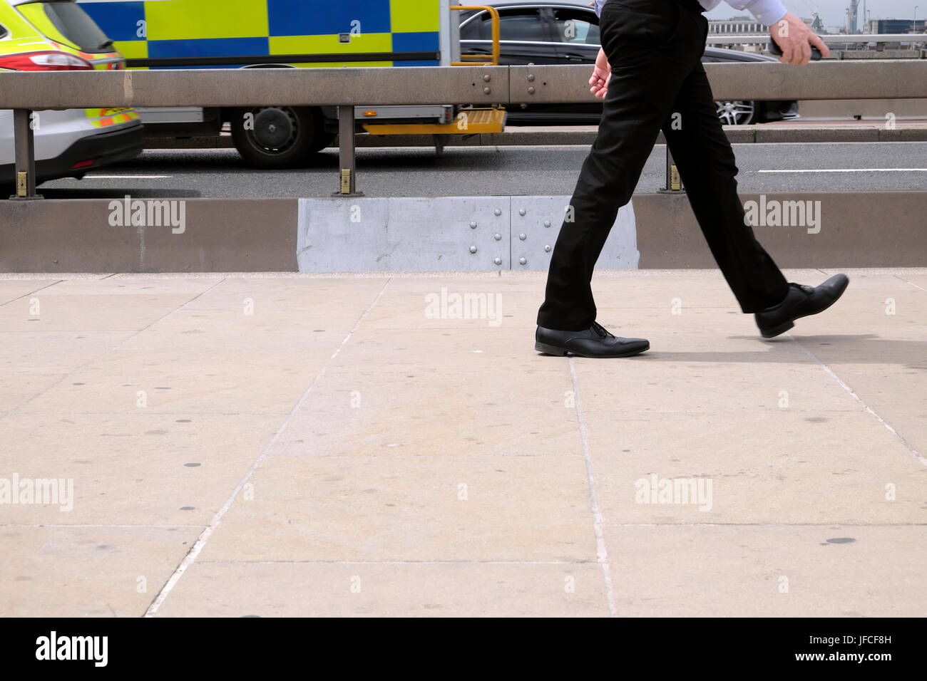 Employé de bureau de banlieue à marcher le long de la chaussée en béton anti-terroriste sur le pont de Londres et l'ambulance UK KATHY DE WITT Banque D'Images