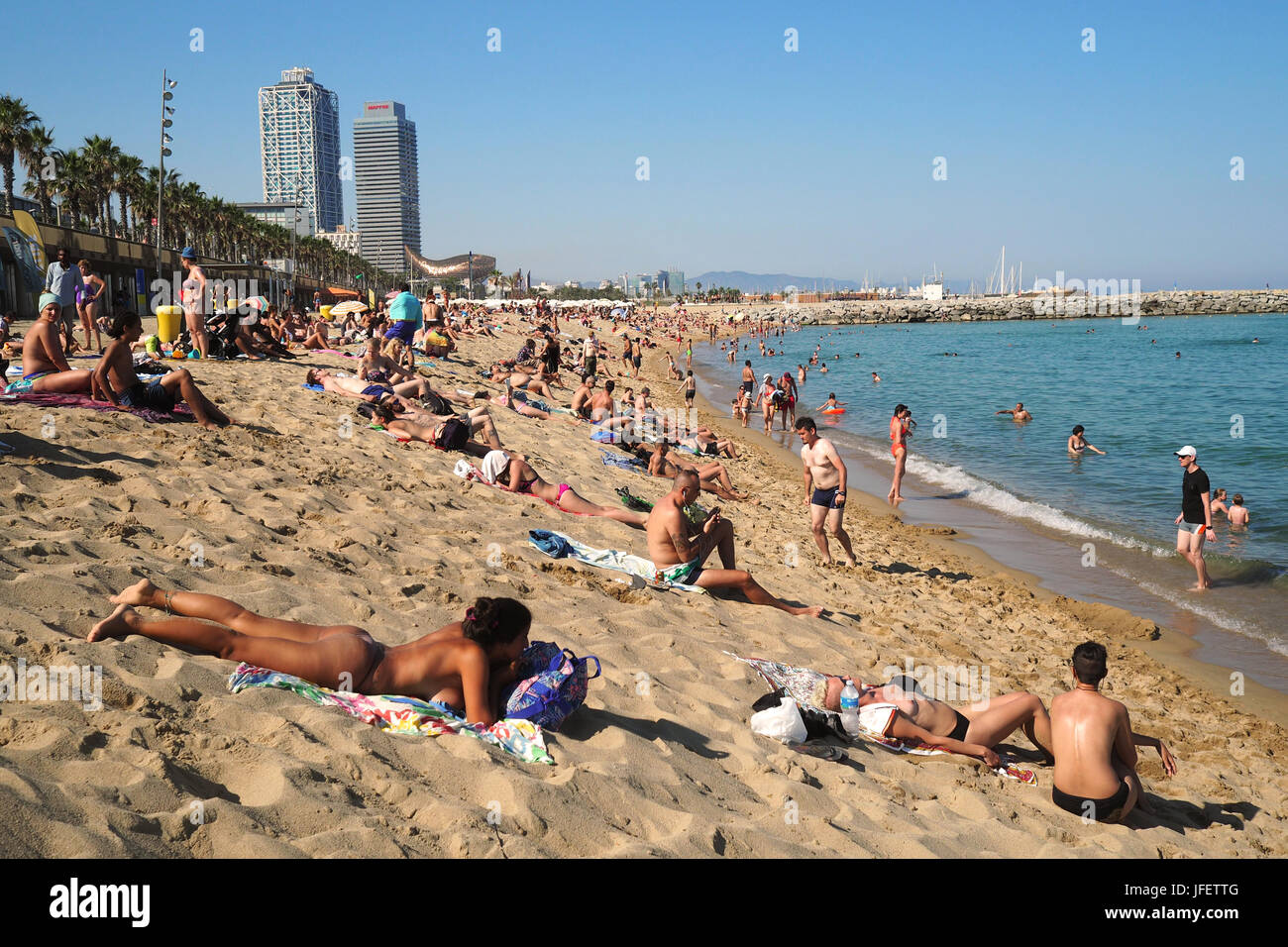 Des foules de gens en train de bronzer sur la plage de Barceloneta ; sur les gratte-ciel en arrière-plan l'hôtel Arts et la Tour Mapfre, Vila Olimpica et Port Olimpic Banque D'Images