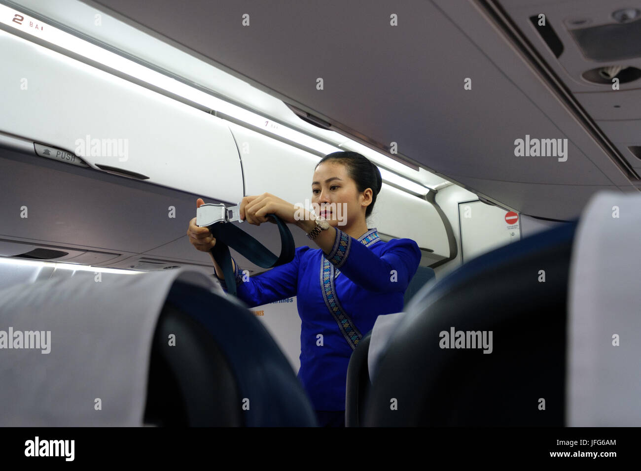 En uniforme d'hôtesse de vol montrant comment utiliser la ceinture de sécurité de l'avion pendant les procédures de sécurité Banque D'Images