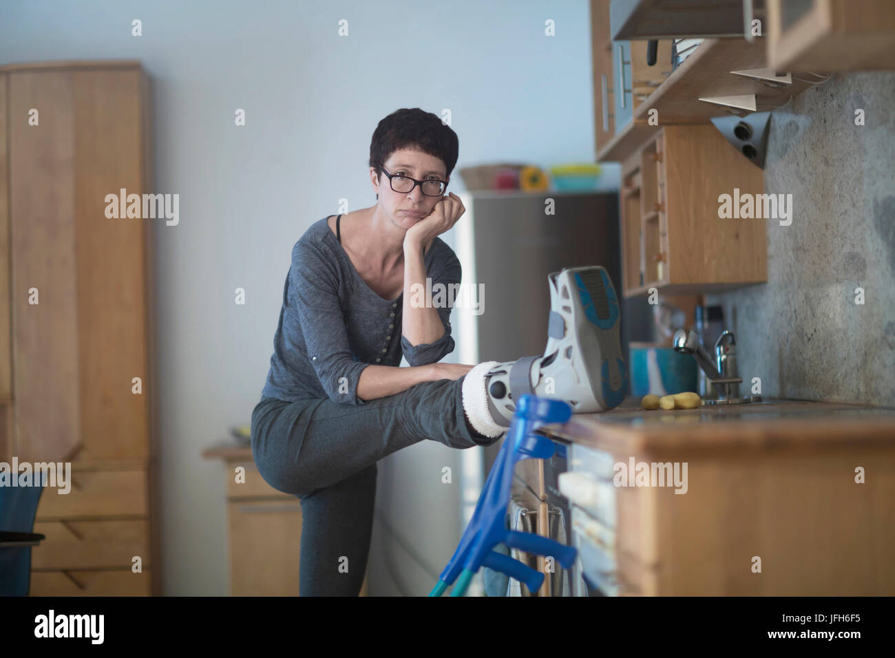 Portrait de femme posant sa jambe cassée sur le plan de travail de cuisine Banque D'Images
