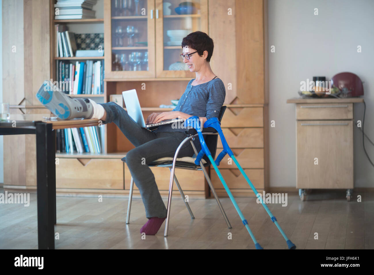 Femme posant sa jambe cassée sur table et à l'aide de l'ordinateur portable sur présidence Banque D'Images