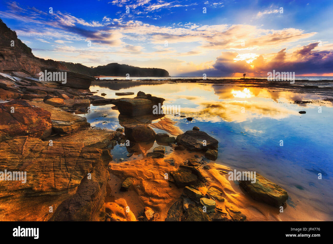 La réflexion des nuages et soleil levant dans la flaque d'eau salée encore durant la marée basse mer ouverture près de falaises de grès Narrabeen pointe à Sydney. Banque D'Images