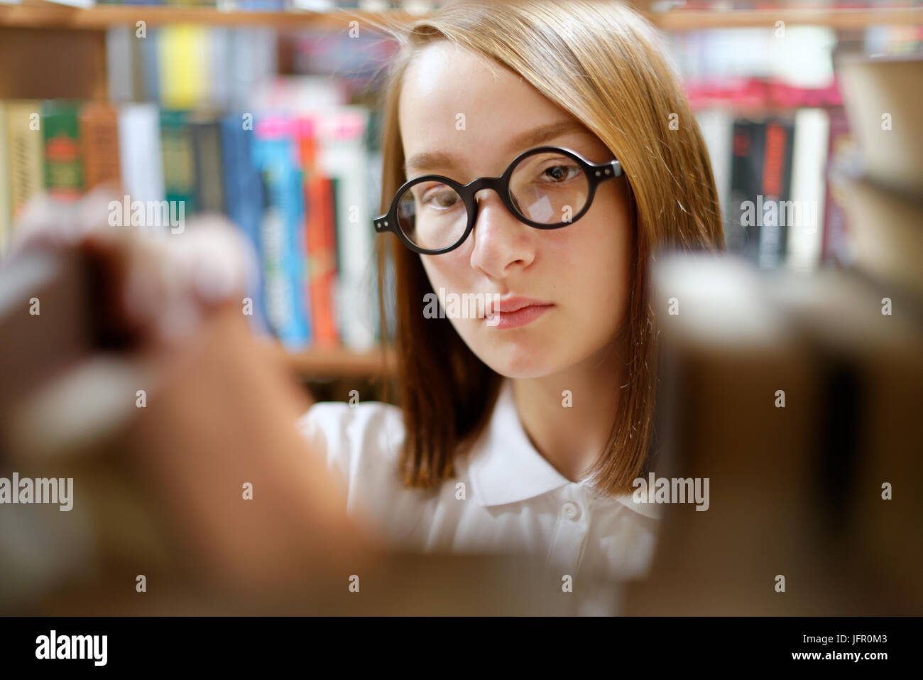 People : jeune fille, étudiante, portant des lunettes, choisit un livre dans une bibliothèque ou une librairie. Banque D'Images