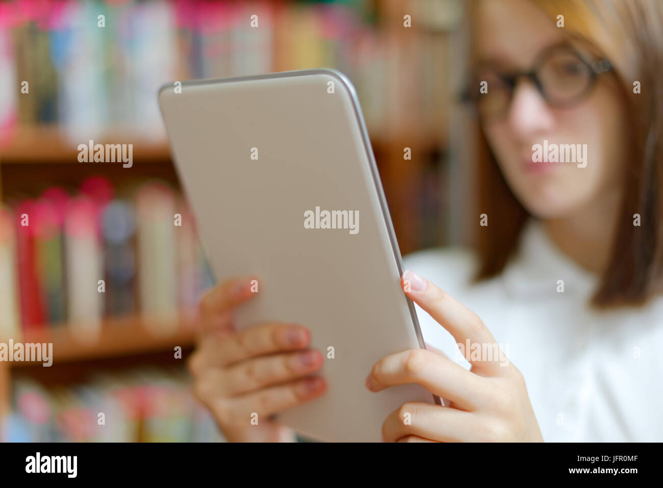 People : jeune fille, étudiante, faisant usage de l'ordinateur tablette ou e-book reader, dans une bibliothèque ou à la librairie Banque D'Images