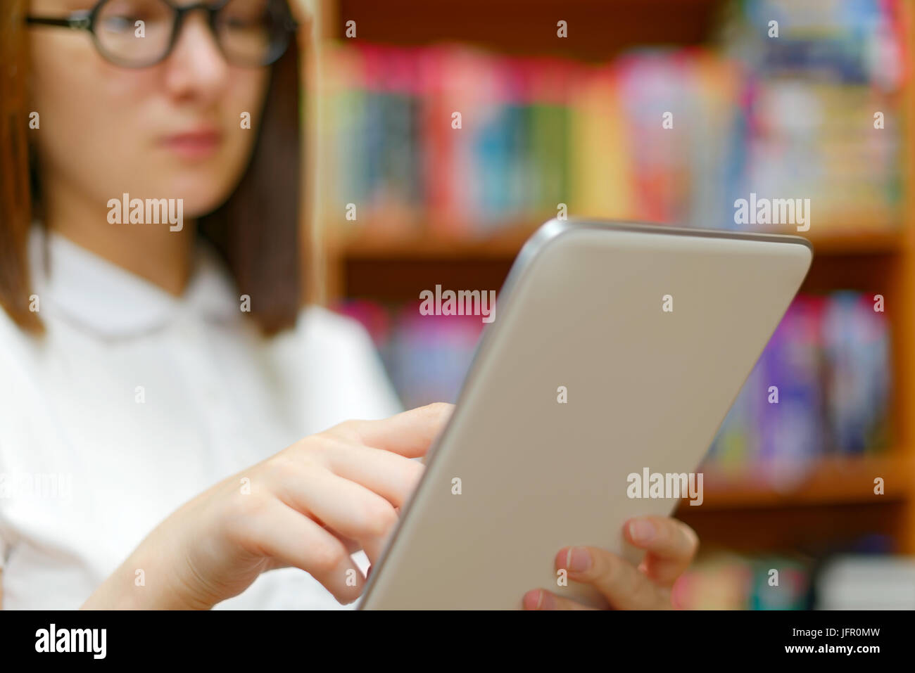 People : jeune fille, étudiante, faisant usage de l'ordinateur tablette ou e-book reader, dans une bibliothèque ou à la librairie Banque D'Images