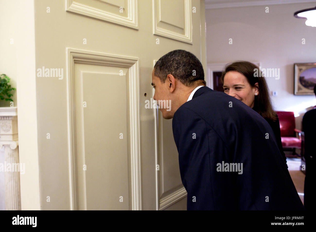 Le président Barack Obama regarde à travers le judas de la porte du bureau ovale comme son secrétaire personnel Katie Johnson montres 3/12/09. Photo Officiel de la Maison Blanche par Pete Souza Banque D'Images