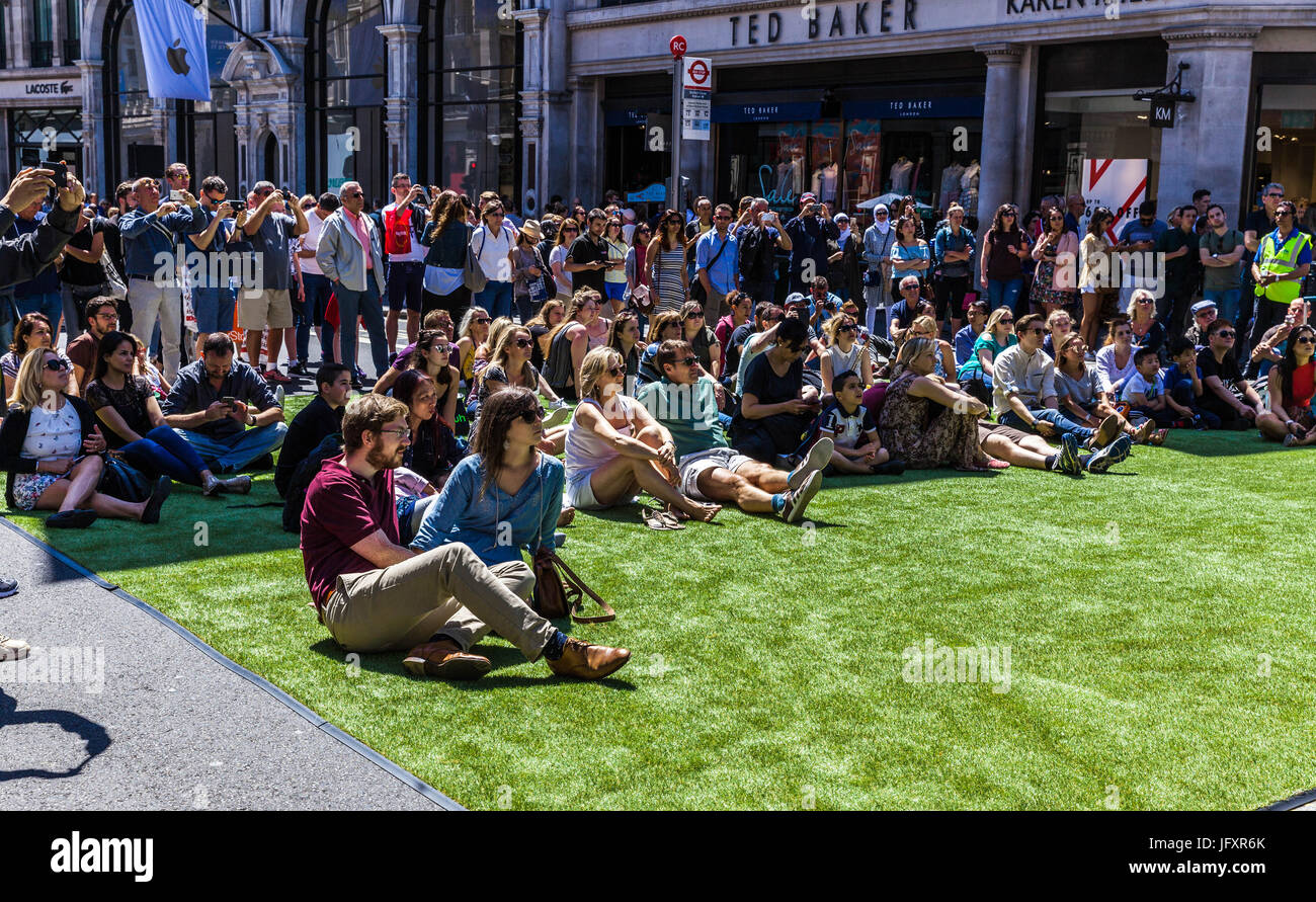 Public assis sur le gazon artificiel et regarder un spectacle, festival libre circulation rues d'été, Regent Street, London, England, UK Banque D'Images