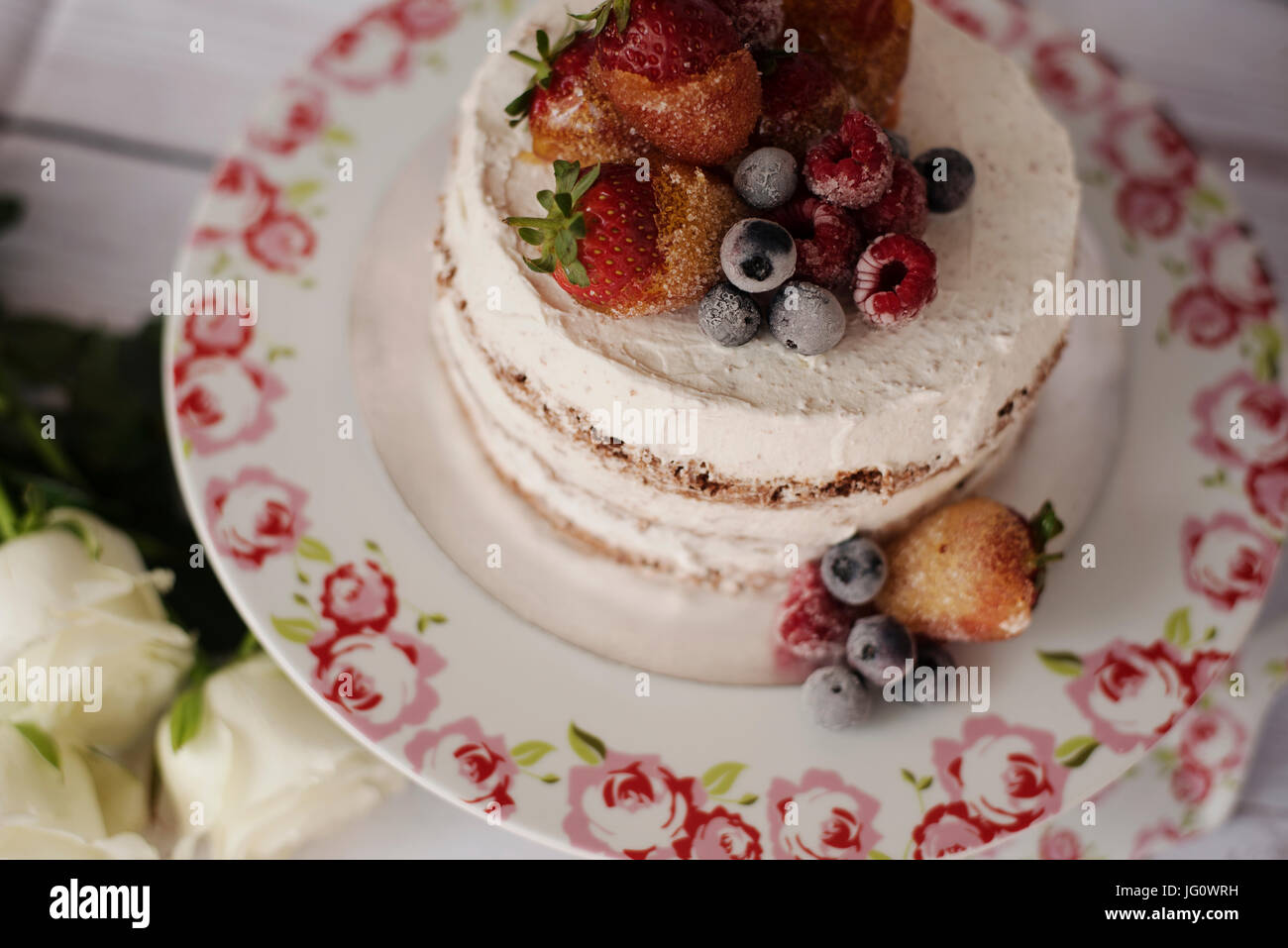 Relations sérieuses gâteau avec des fruits caramélisés - fraises, bleuets, framboises. Sponge cake crème floral en haut plateau, bac. Des roses blanches, backg rustique Banque D'Images