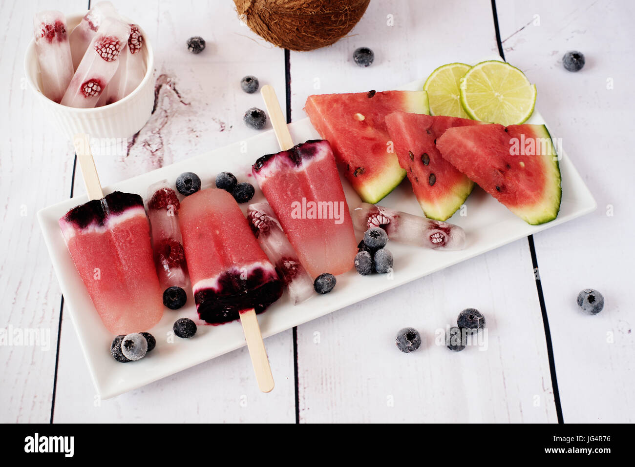 Les sucettes glacées des pastèques, le lait de coco, citron vert, framboises et bleuets. Glace sur un plateau rectangulaire rectangle blanc, glace aux framboises. L Banque D'Images