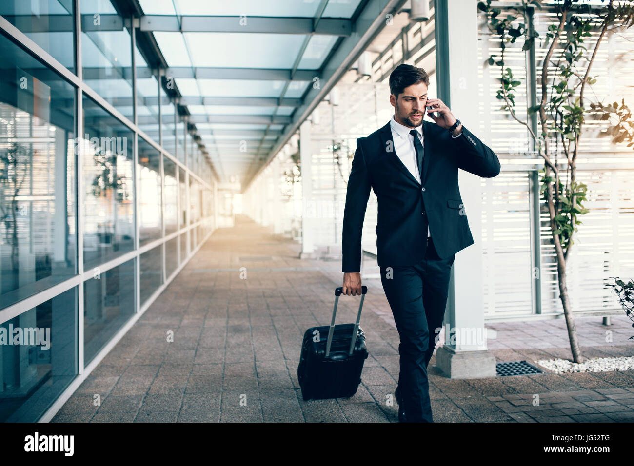 Beau jeune homme en voyage d'affaires à marcher avec ses bagages et parler sur téléphone cellulaire à l'aéroport. Hommes d'affaires faisant appel téléphonique. Banque D'Images
