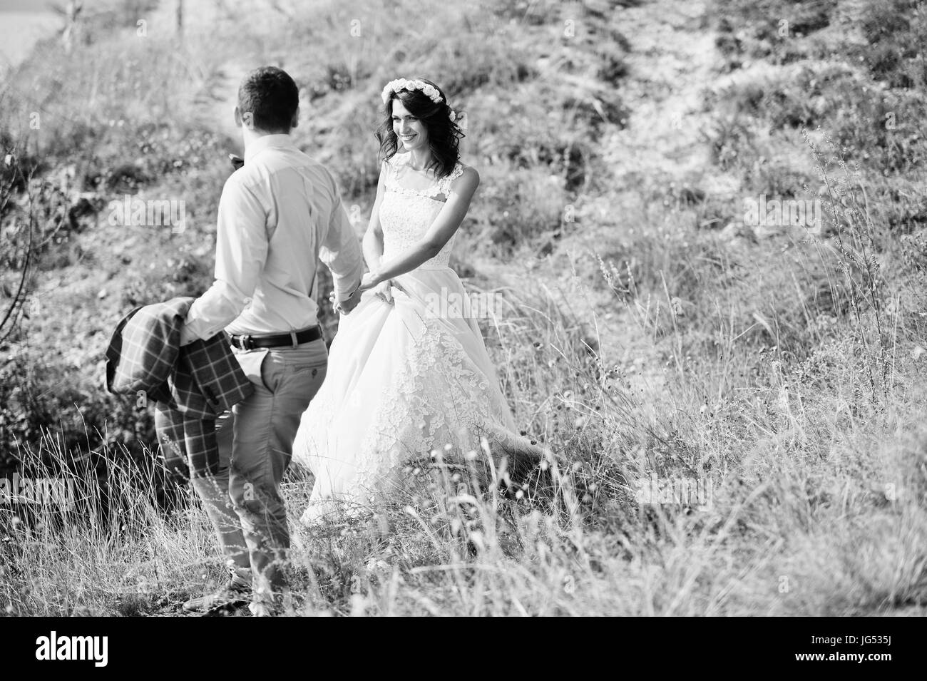 Beautiful wedding couple en train de marcher et profiter de la compagnie de l'autre dans un quartier avec de grands rochers herbe sèche. Photo en noir et blanc. Banque D'Images