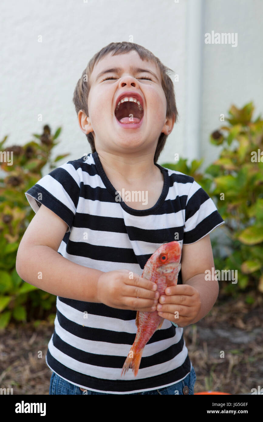 Un jeune garçon riant tout en tenant un poisson, France. Banque D'Images