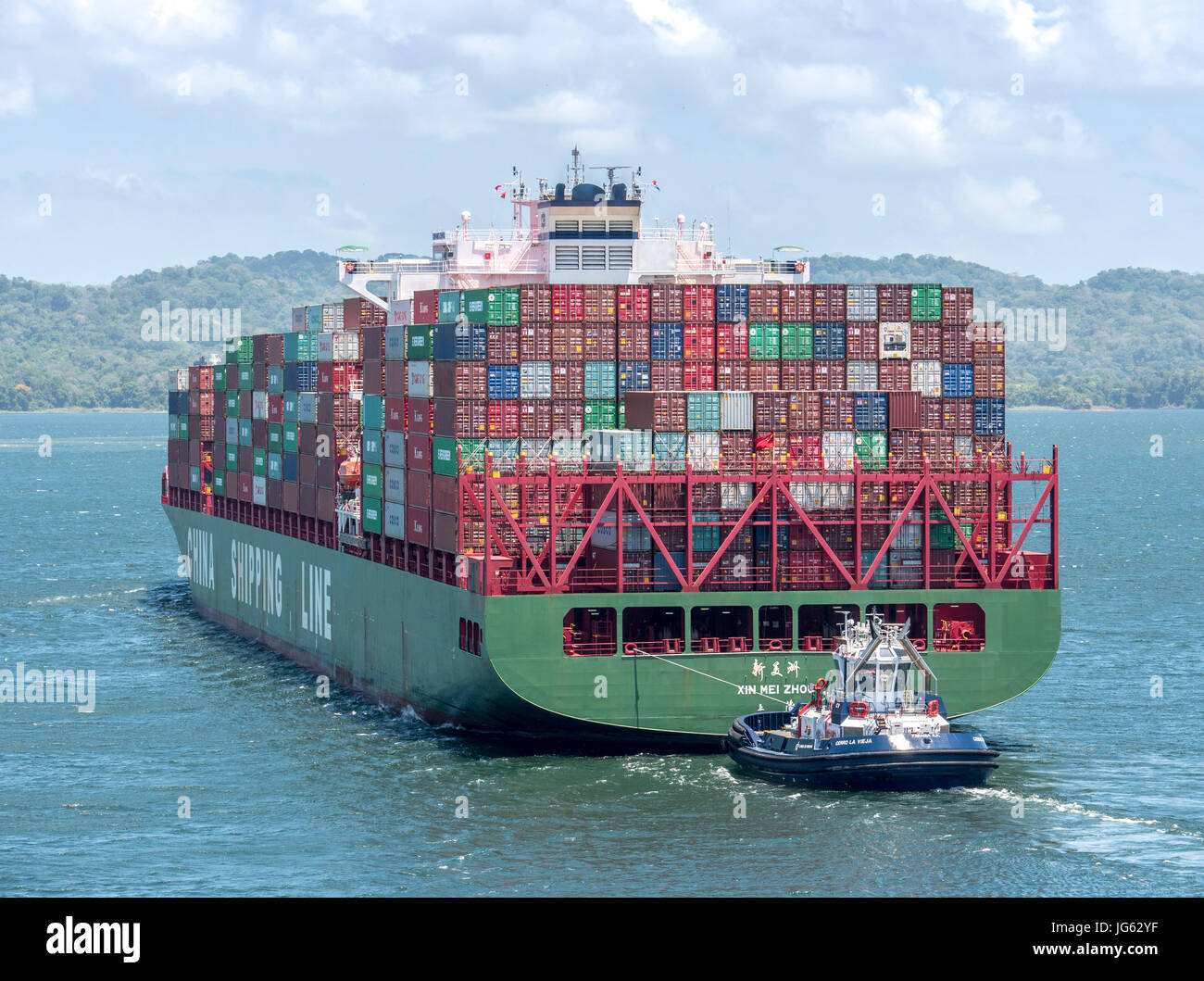 Un grand porte-conteneurs Xin Mei Zhou, de l'Chine voyage ligne passant par le lac Gatun du Canal de Panama, dirigé par un remorqueur Banque D'Images