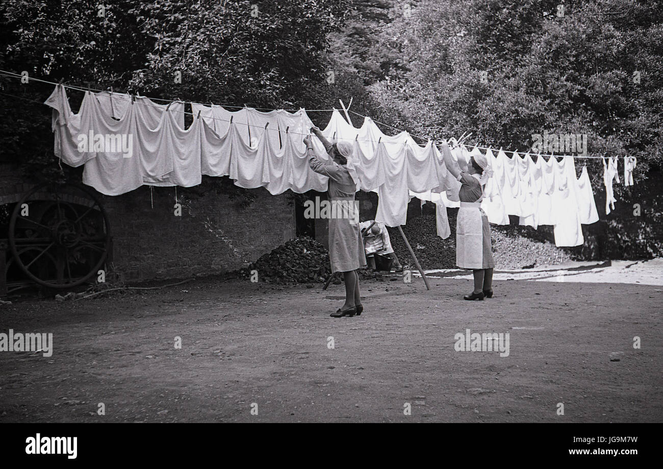 1940, historique, deux employées de maison suspendues à la lessive sur une corde à linge à l'extérieur dans le domaine de Stanstead Hall, Essex, maison de Sydney Courtauld, Lady Butler. Sa maison de campagne est devenue la maison pour les enfants en bas âge évacués de l'école infantile Wellgarth, Hamptead Garden Suburbs après qu'elle a été détruite par une mine terrestre pendant le Blitz de la seconde Guerre mondiale. Banque D'Images