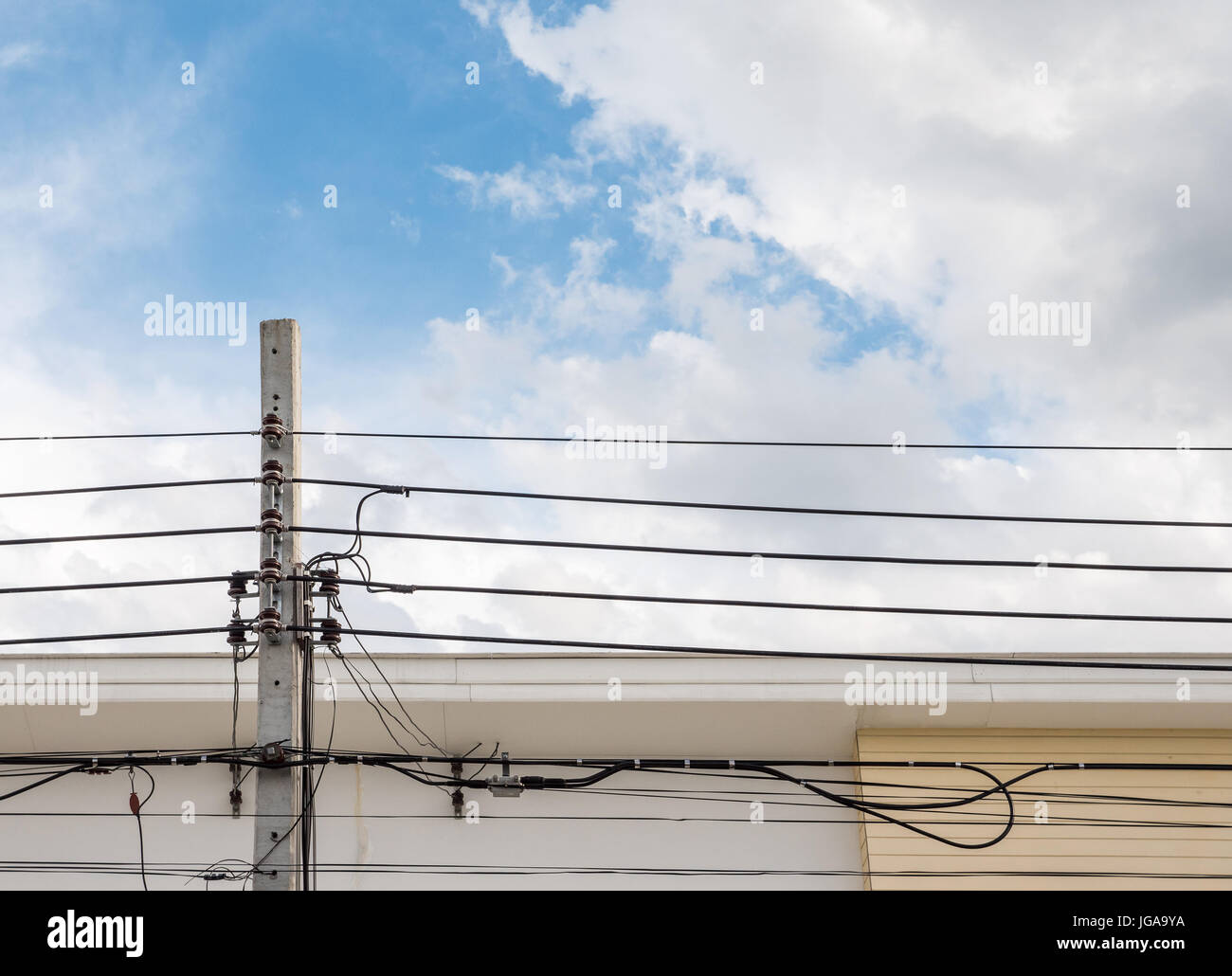 Pôle électrique avec le câble de communication en face de la maison moderne en zone urbaine. Banque D'Images